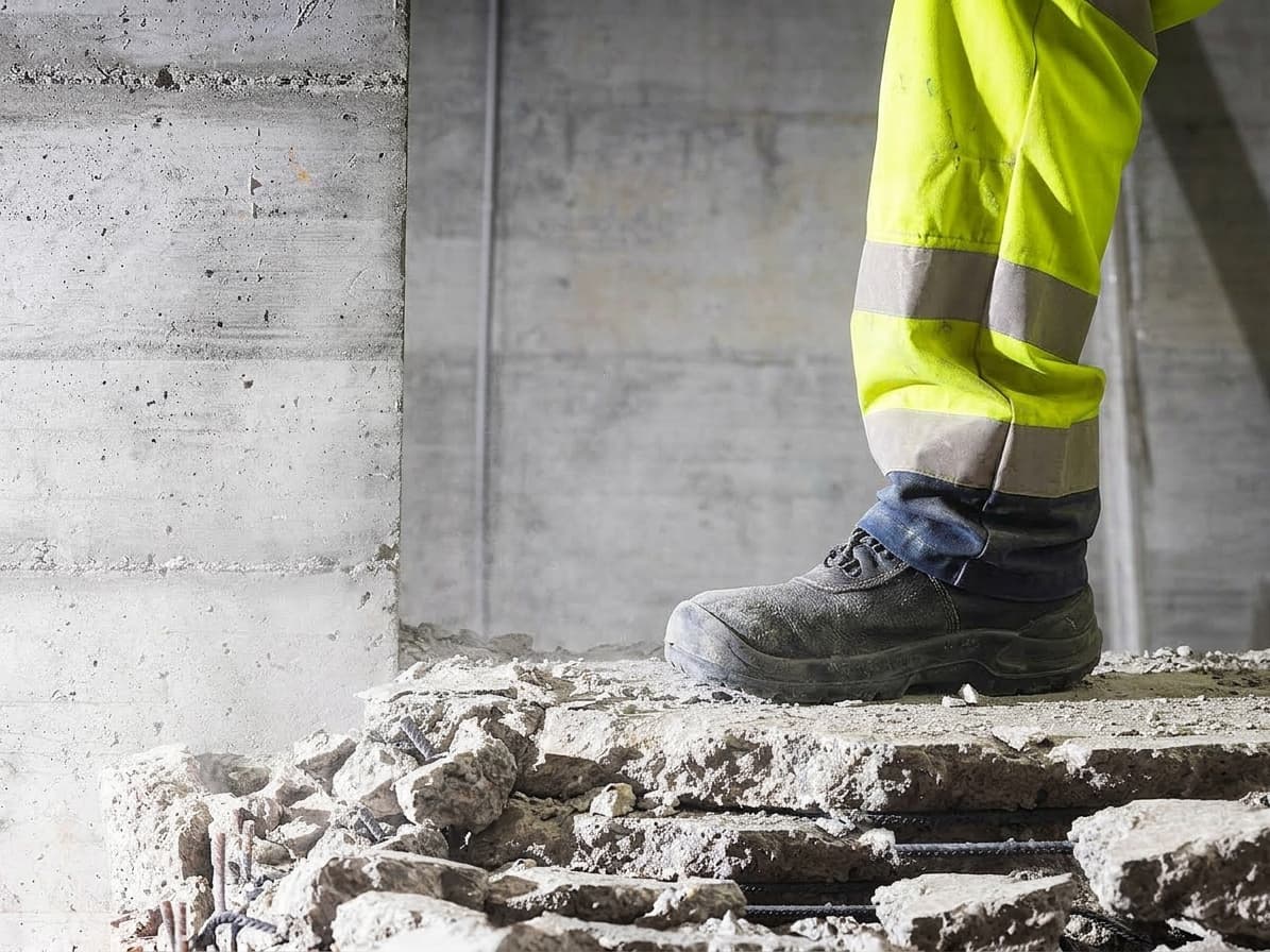 Bauarbeiter in Warnschutzhose steht auf einer aufgebrochenen Betondecke mit freiliegender Bewehrung.